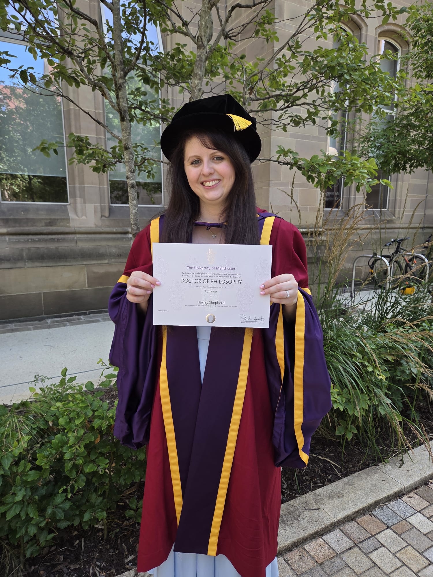 Picture of Hayley in a graduation robe holding her PhD certificate