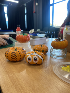 Three mini pumpkins on a table, painted with eyes and various patterns.