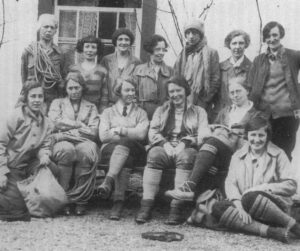 Black-and-white photograph of a group of 13 women wearing outdoor and climbing attire, seated and standing in two rows outside a building, representing members of the Pinnacle Climbing Club.