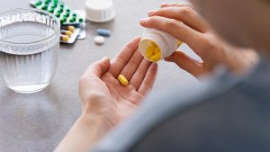 A close up of a person shaking tablets out of a pill bottle.