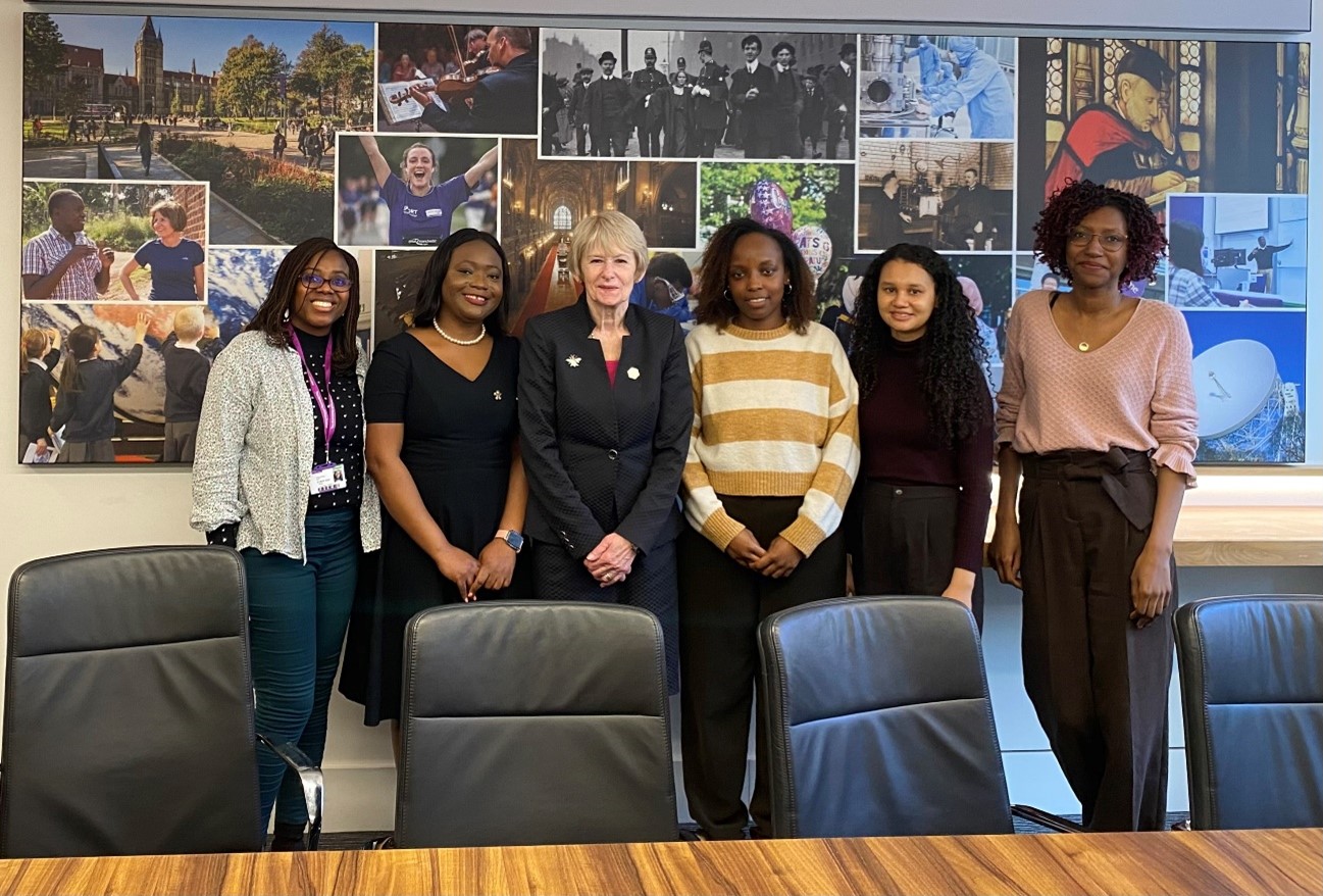 The current 100 Black Women Professors Now cohort during their first meeting with President and Vice Chancellor, Nancy Rothwell in March 2024. THey all stand in front of a wall of University of Manchester pictures.