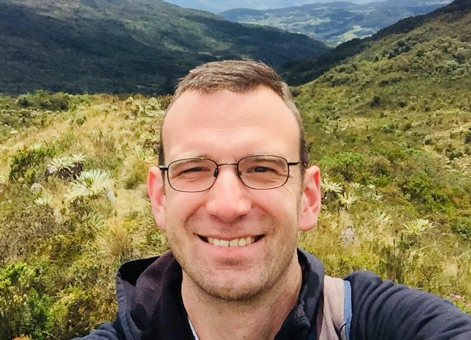 Philip Harrison smiling, taking a selfie in front of a mountain range