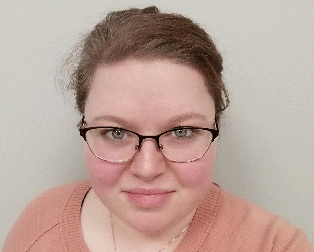 Louise Courtney looking into the camera, wearing glasses and a peach coloured jumper.