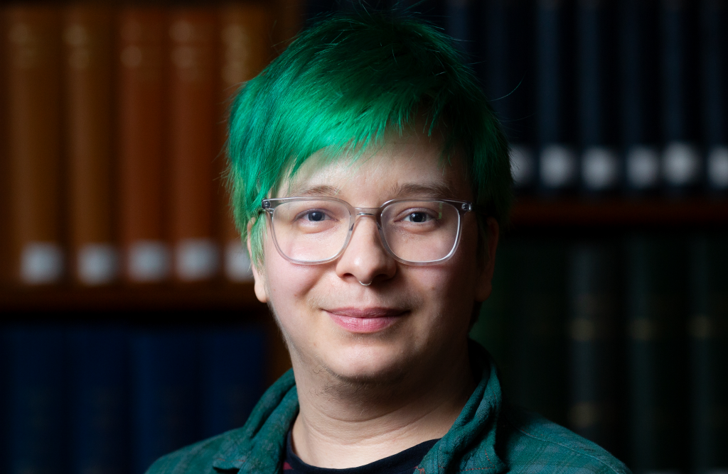 Bean Sharp, a person with green hair and clear glasses, smiles at the camera.