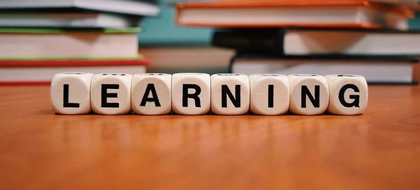 Wooden blocks spelling out the word 'LEARNING' arranged in a row on a wooden surface, with several books stacked in the background.