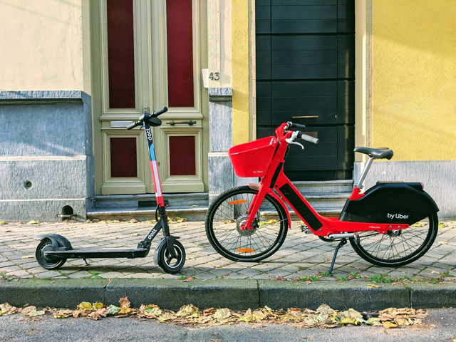 An electric scooter and bicycle in front of pastel coloured houses