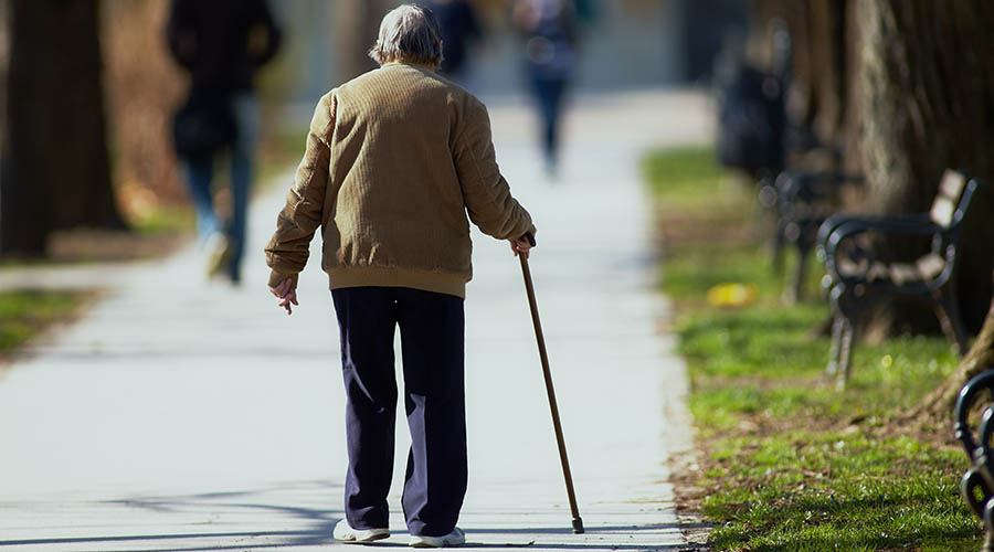 An elderly man walking in the park using a walking stick