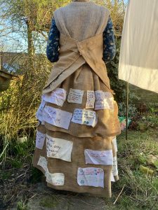 A handmade dress made of repurposed sacks, adorned with handwritten pledges promoting sustainable fashion and second-hand shopping.