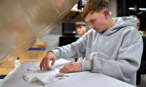 Person aligning a design on a white T-shirt under a heat press in a workshop setting