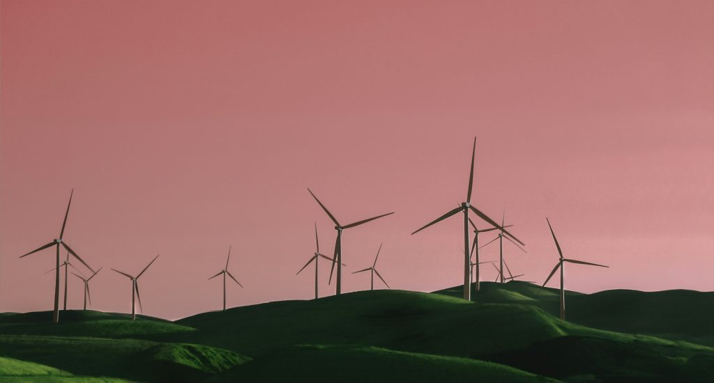 Pink filled skies with a landscape of white windmills on green hilltops sporadically.