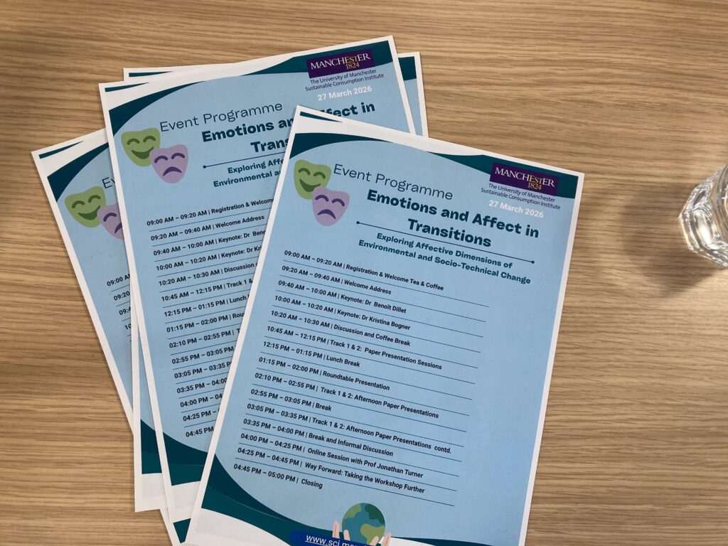 Event programmes for “Emotions and Affect in Transitions” laid on a wooden table beside a glass of water at the University of Manchester workshop.