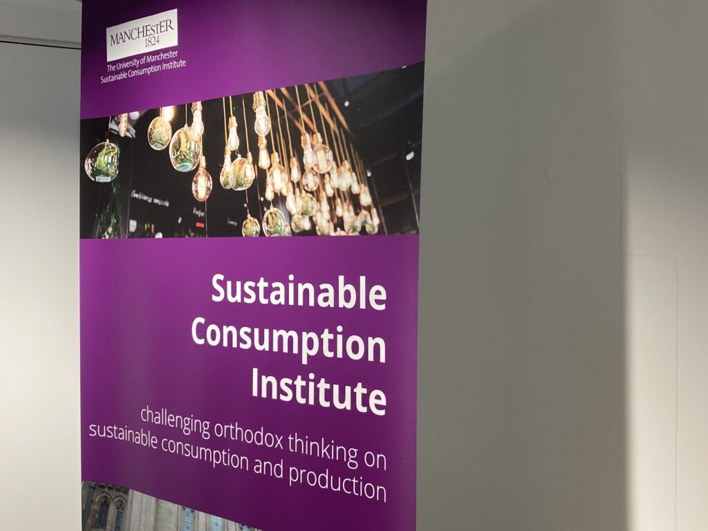 A purple banner for The University of Manchester’s Sustainable Consumption Institute, featuring hanging light bulbs with small plants inside and the tagline “challenging orthodox thinking on sustainable consumption and production.”